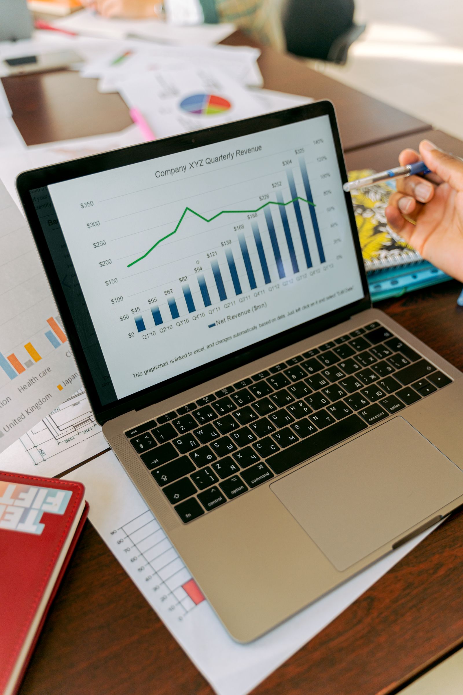 A real laptop displaying a quarterly revenue graph beside printed reports